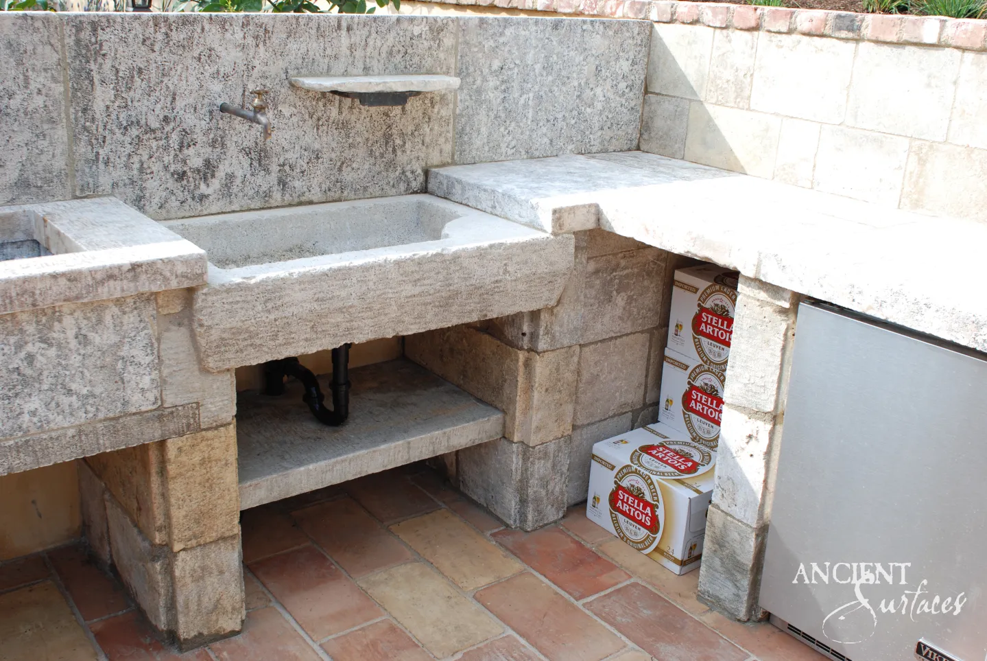 Deep rectangular reclaimed limestone trough sink built into a rustic outdoor stone kitchen counter